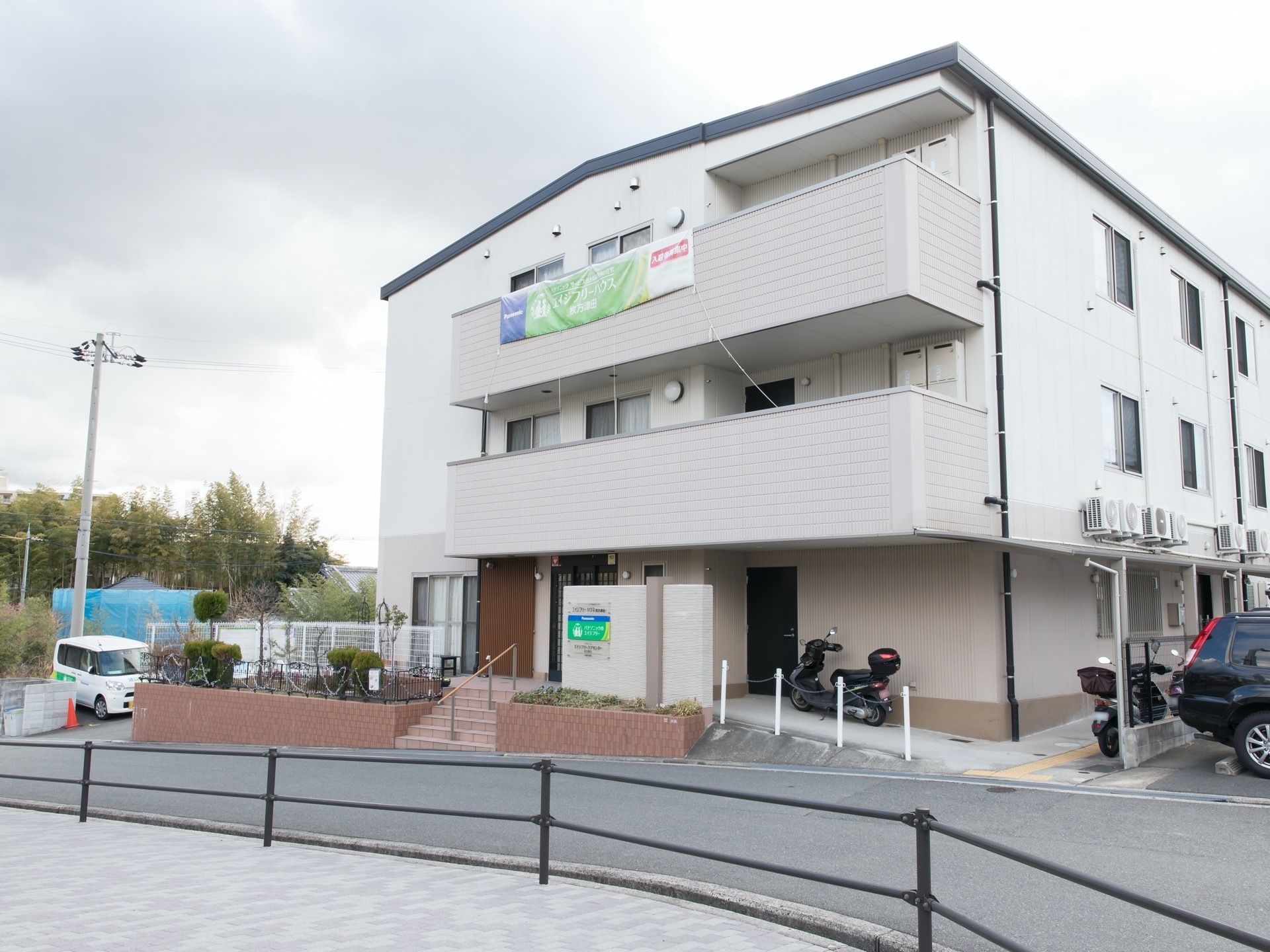 施設は、鉄骨造りの３階建てである。外壁は、白となっている。玄関への通路は、スロープの通路と階段が設置されている。