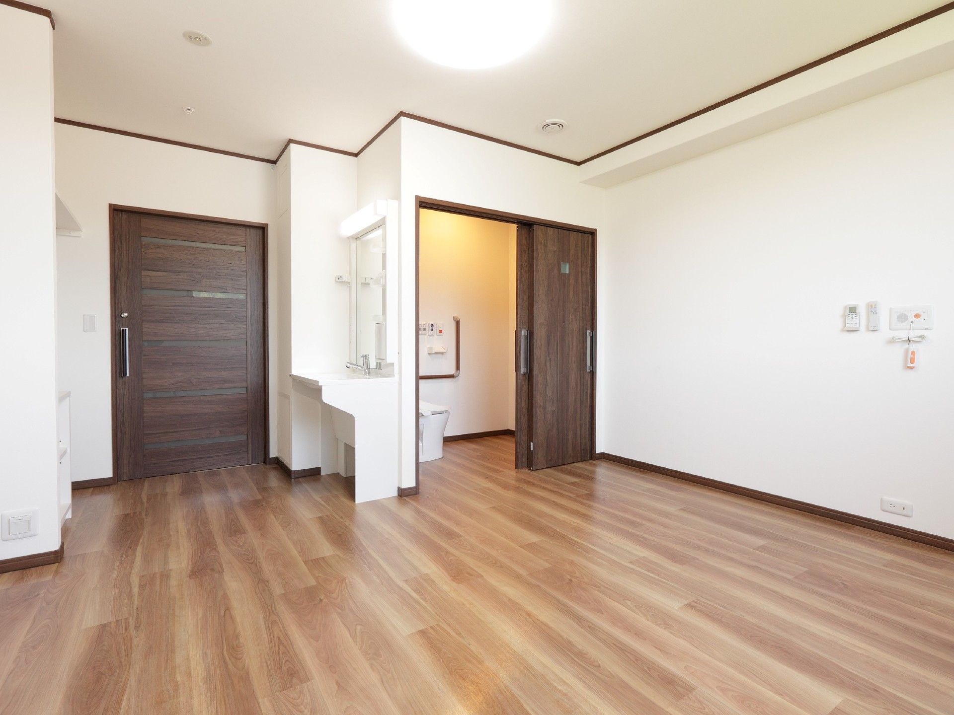 大きな引き戸が付いたトイレと洗面所が付いた居室は家具が置かれる前の様子。壁には緊急通報装置も付いている。