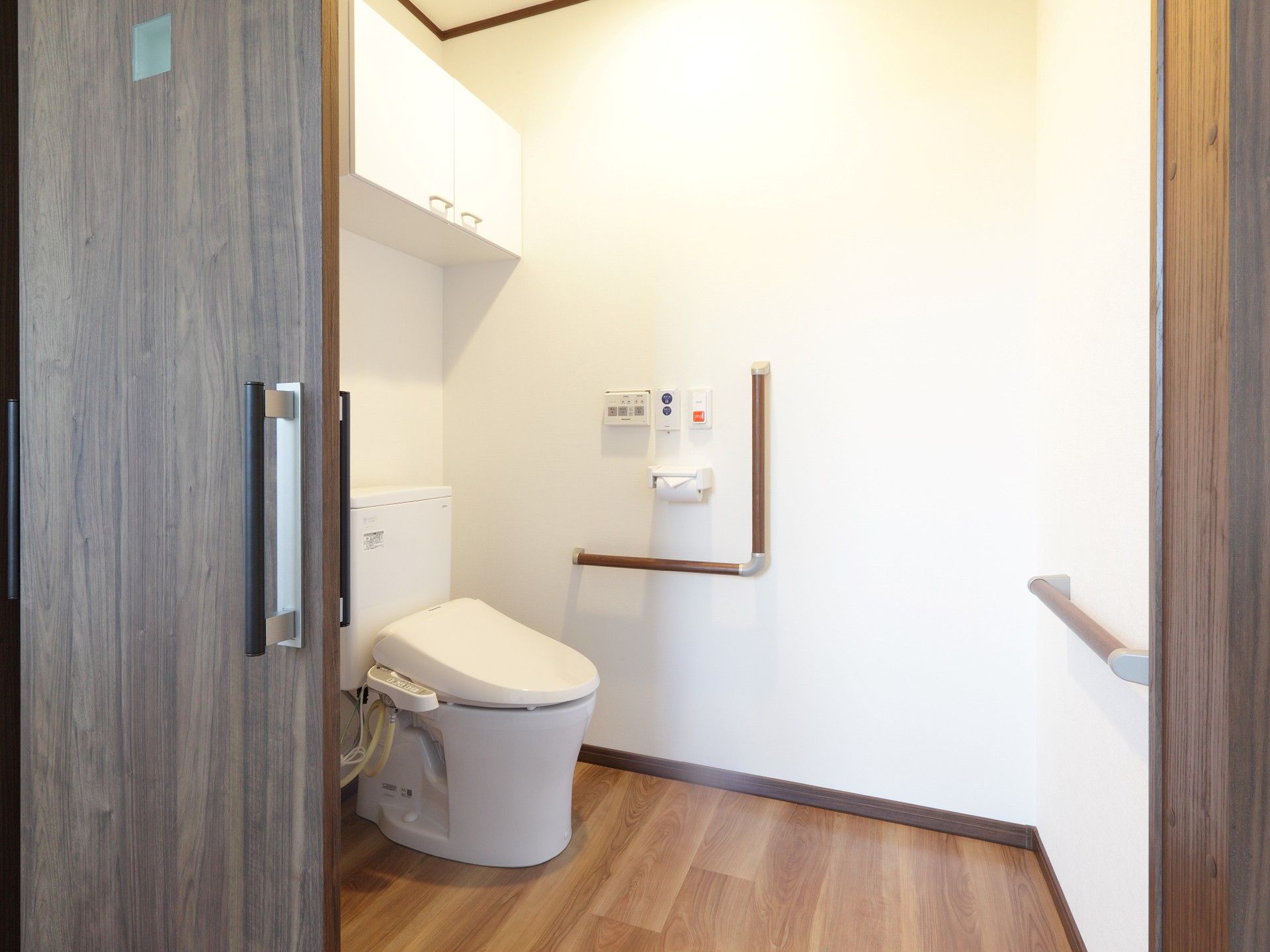 複数の手すりが設置されたトイレは広く、大きな棚や呼び出しボタンも付いている。