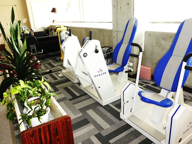 白とブルーのリハビリマシンがそろった共有スペースには観葉植物が飾られている。