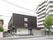 住宅地にある建物はグレー系で周辺の景観によくなじんでいる。３階建てでベランダや駐車場がある。