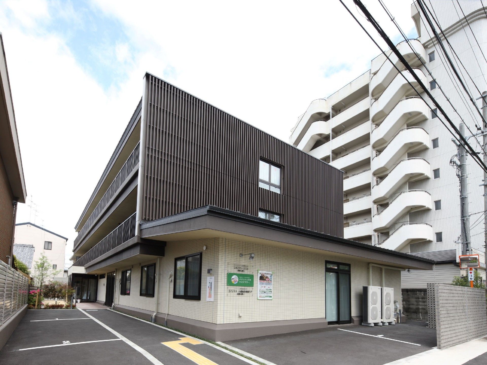 グレーと白の建物は3階建てで、玄関部分には屋根が付き、ベランダも設置されている。