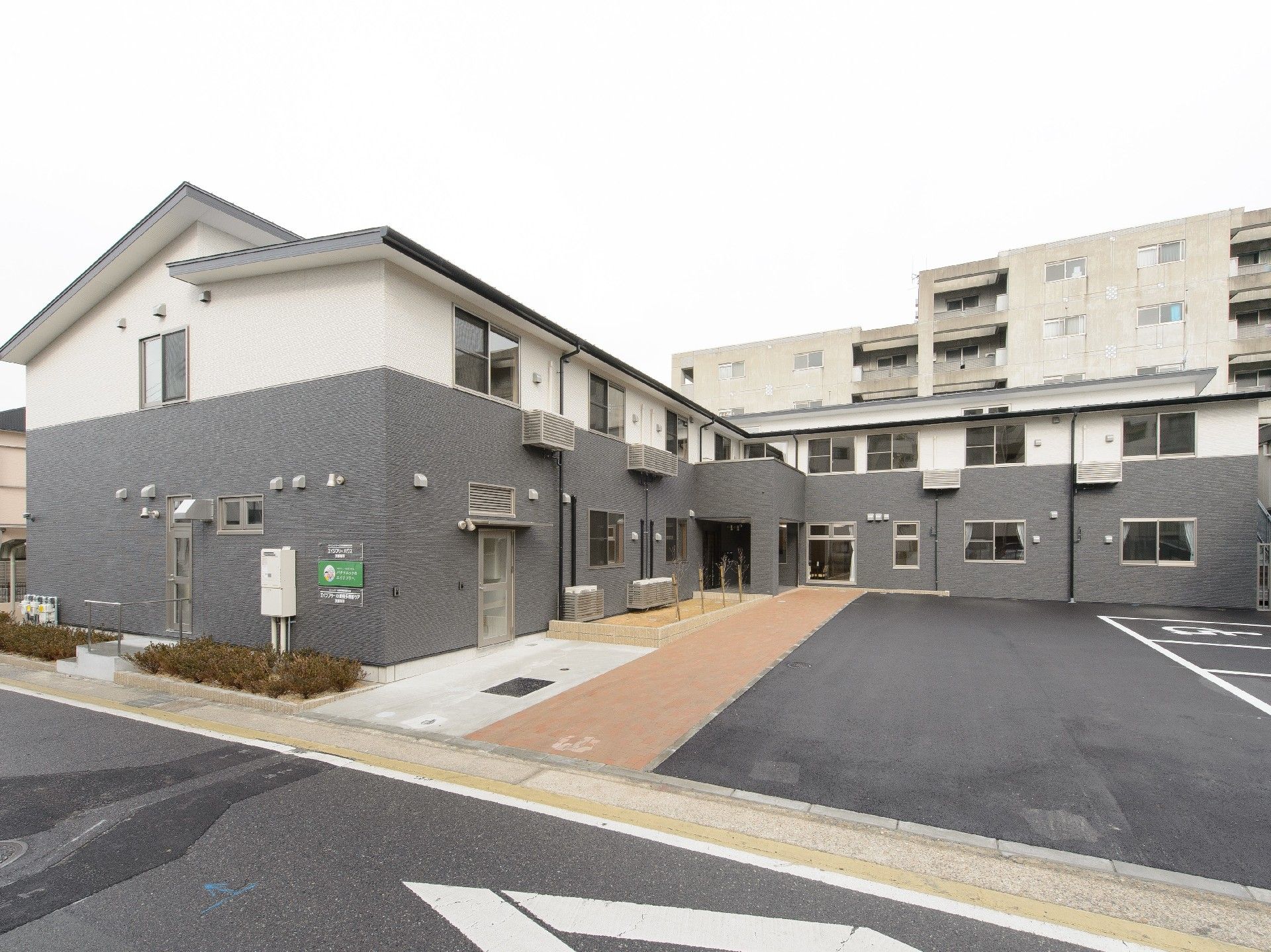 ２階建ての建物。グレーを基調とし、出入り口と１階部分には屋根が付いている。駐車場も広い。