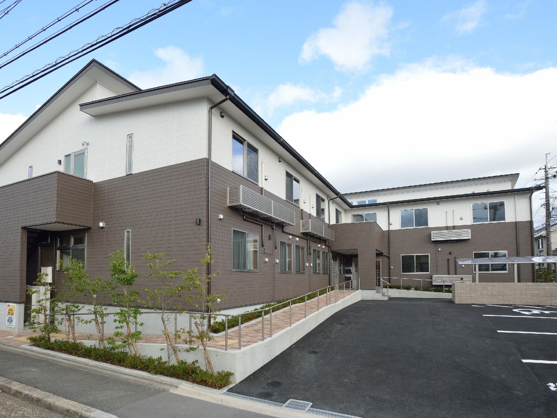 白とグレーの2階建て他の建物。玄関先には屋根があり、木も植えられている。