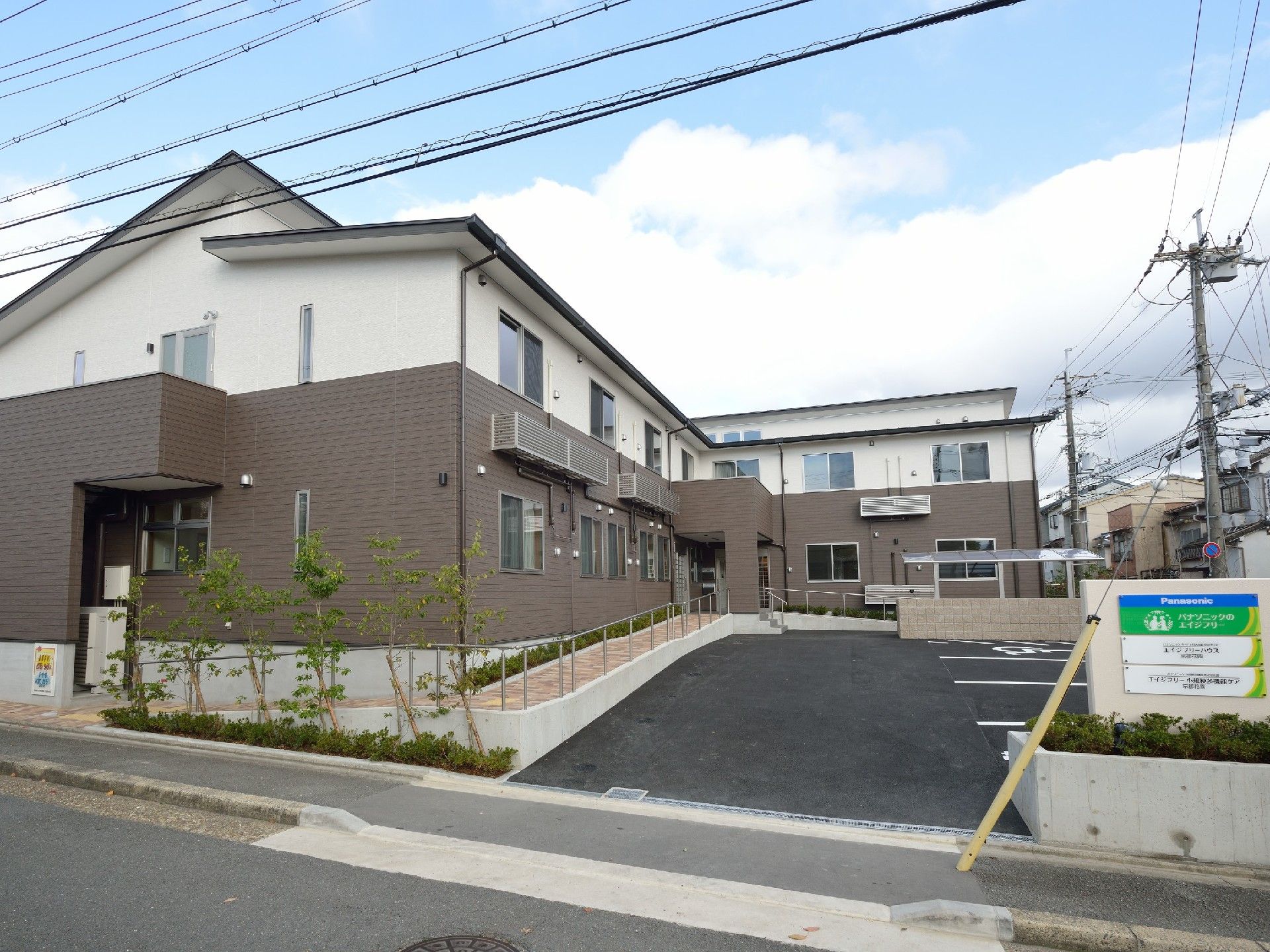 駐車スペースがたくさんあり、日当たりもよい。エル字型の建物は2階建てで白とグレー。