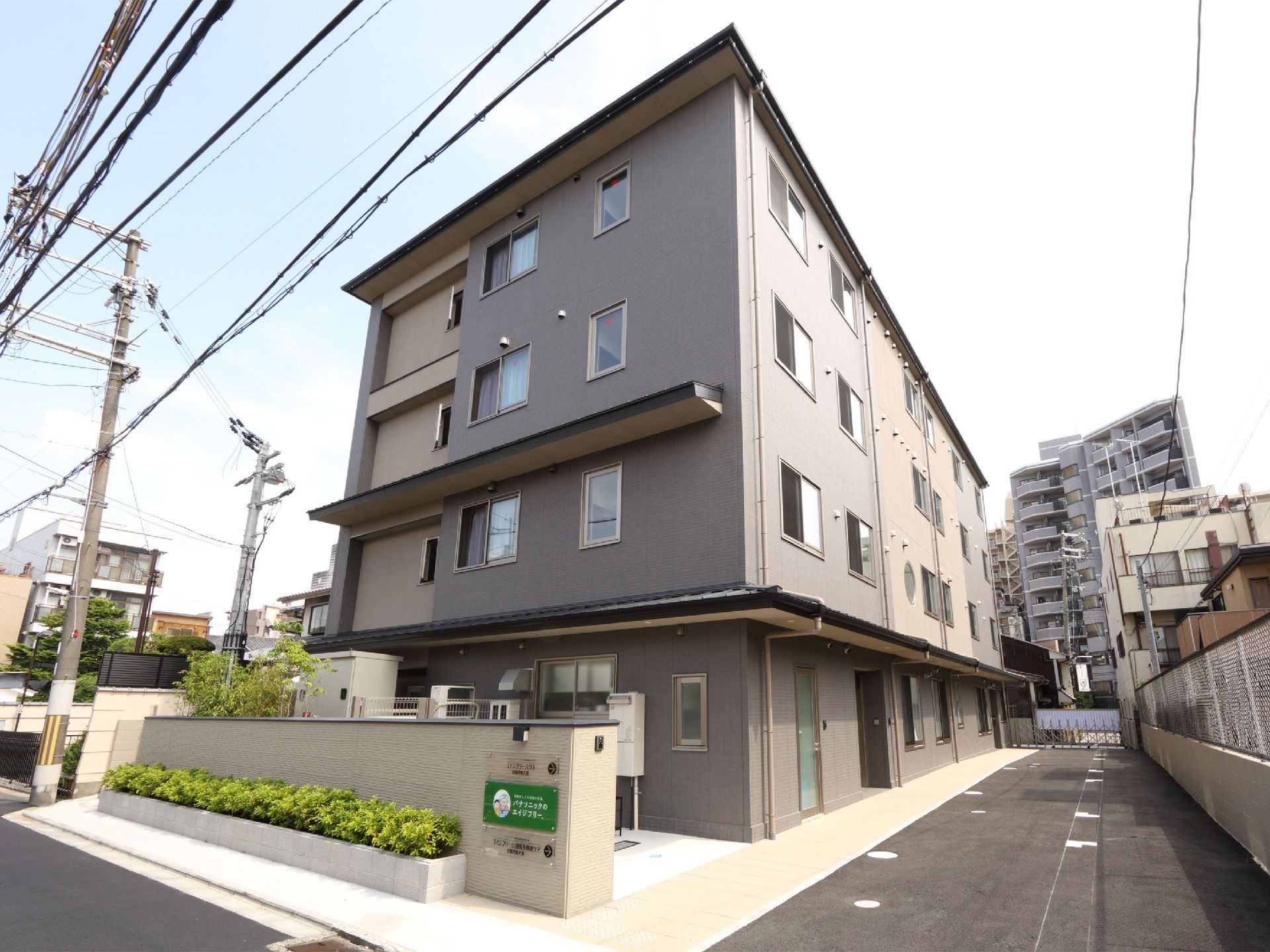 ダークブラウンの4階建ての建物。周辺にはマンションなども建ち、街中にあることがうかがえる。