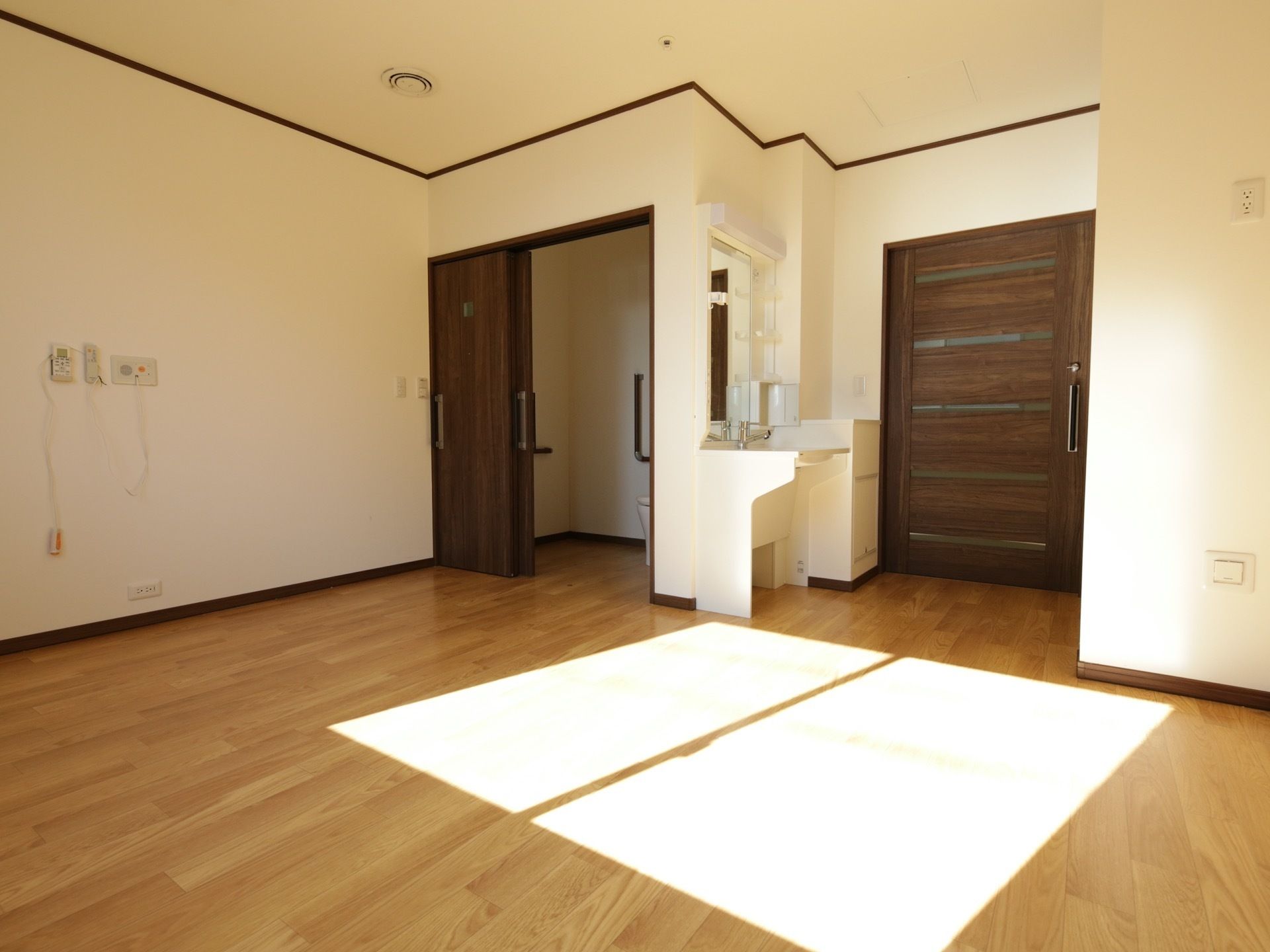 居室は、明るいフローリングにブラウンの建具を組み合わせた内装で、木材の存在が際立つ。壁にはナースコールが設置されている。
