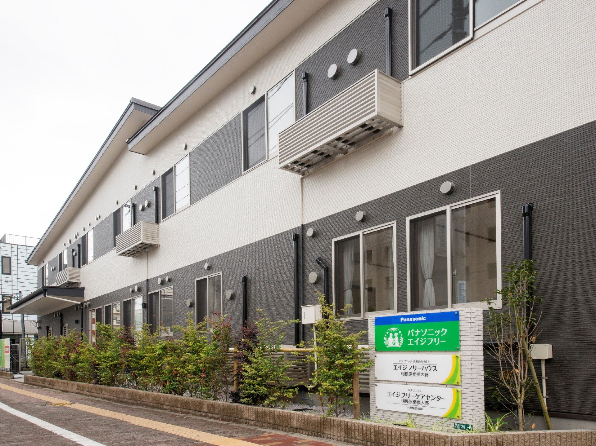 2階建ての白とダークグレーの建物。玄関には屋根が付き、2階には窓がたくさんある。