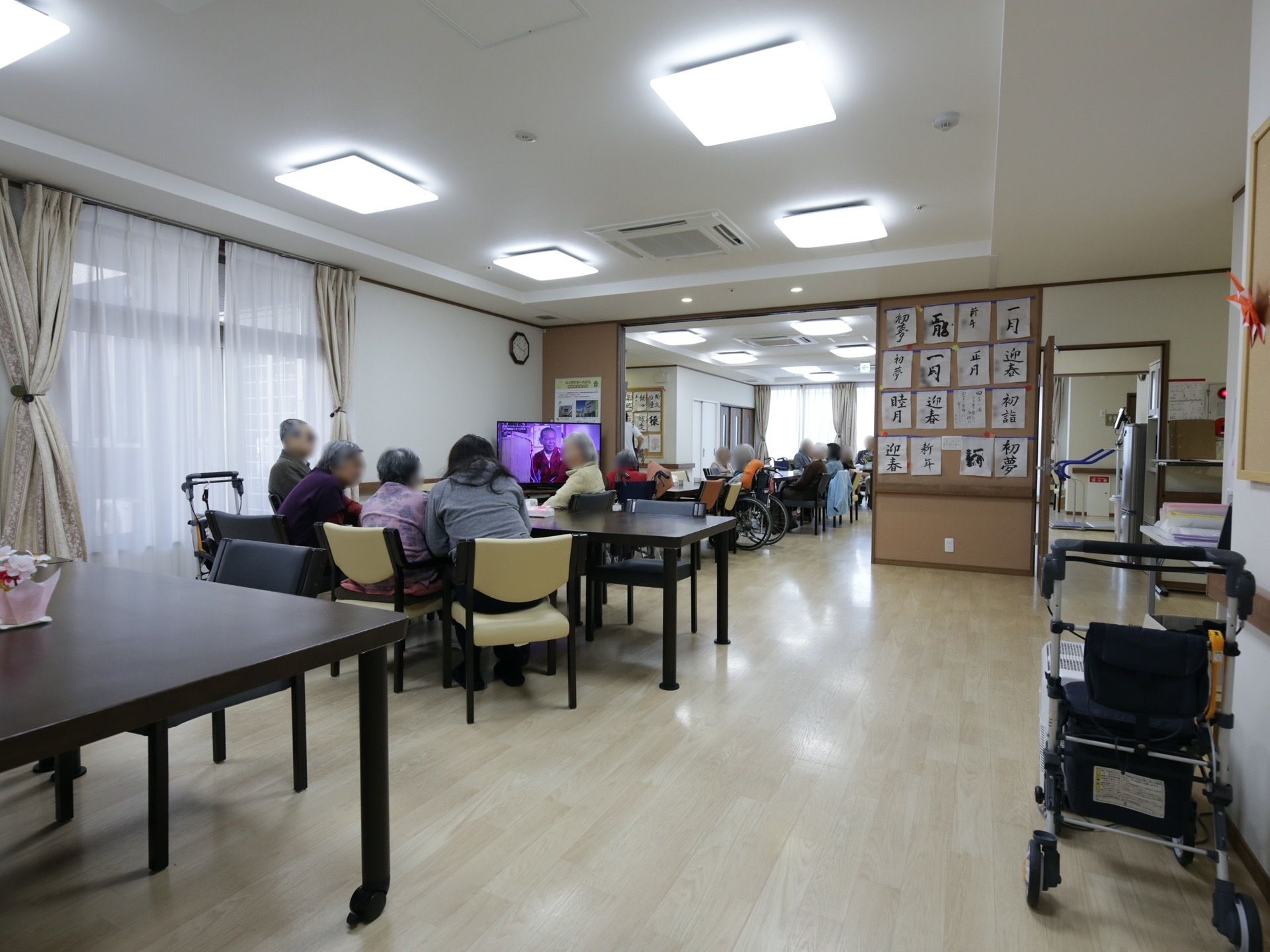 食堂は２つの部屋に分かれているが、境目のパーテーションは大きく開け放たれている。入居者様がテレビの前に集まっている。