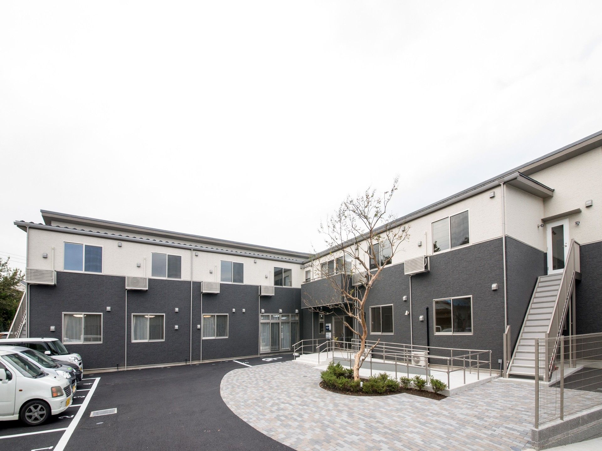 2階建ての建物。1階部分はダークグレー、2階部分は白で、側面には避難用の屋外階段もついている。