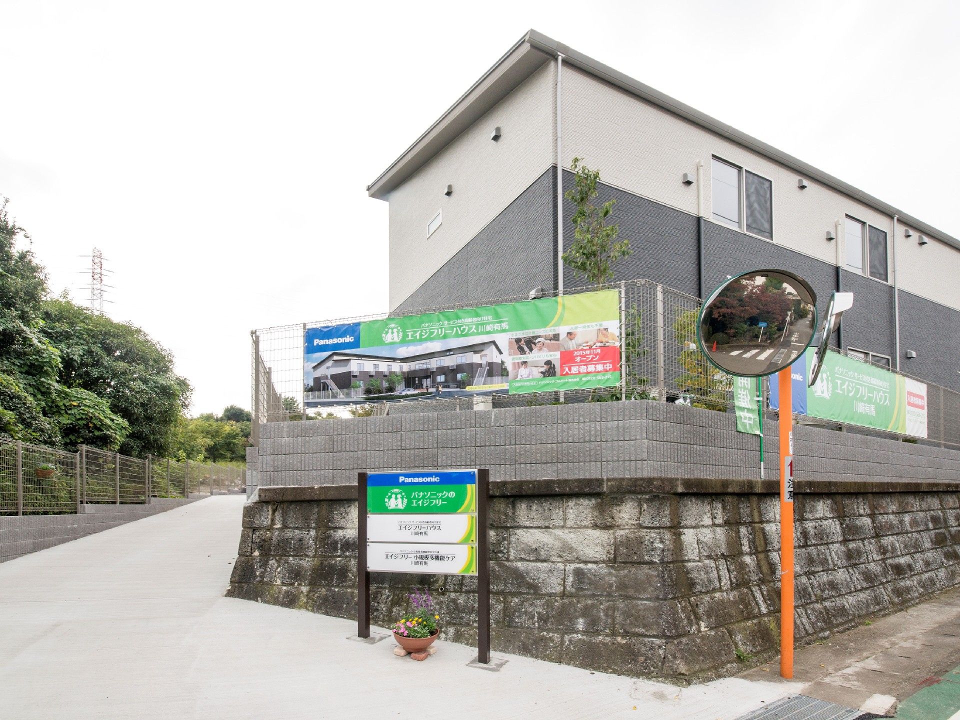 2階建ての建物は自然に囲まれ、近くに住宅や併設事業所の案内看板がある。