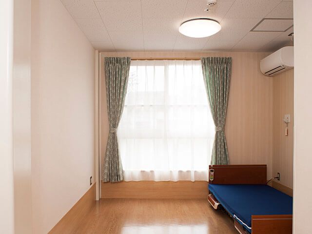エアコンや介護ベッドが付いたフローリングの居室。壁には緊急通報装置を設置している。