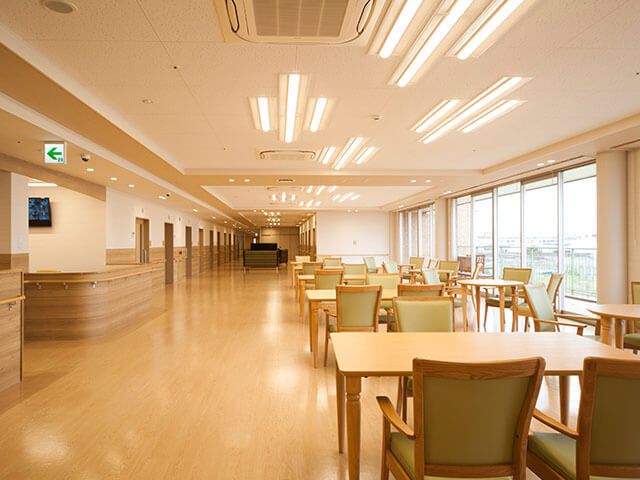 木製のダイニングテーブルセットは4人掛け。窓に近い場所にテーブルセットが並び、左には居室が並ぶ廊下が見える。