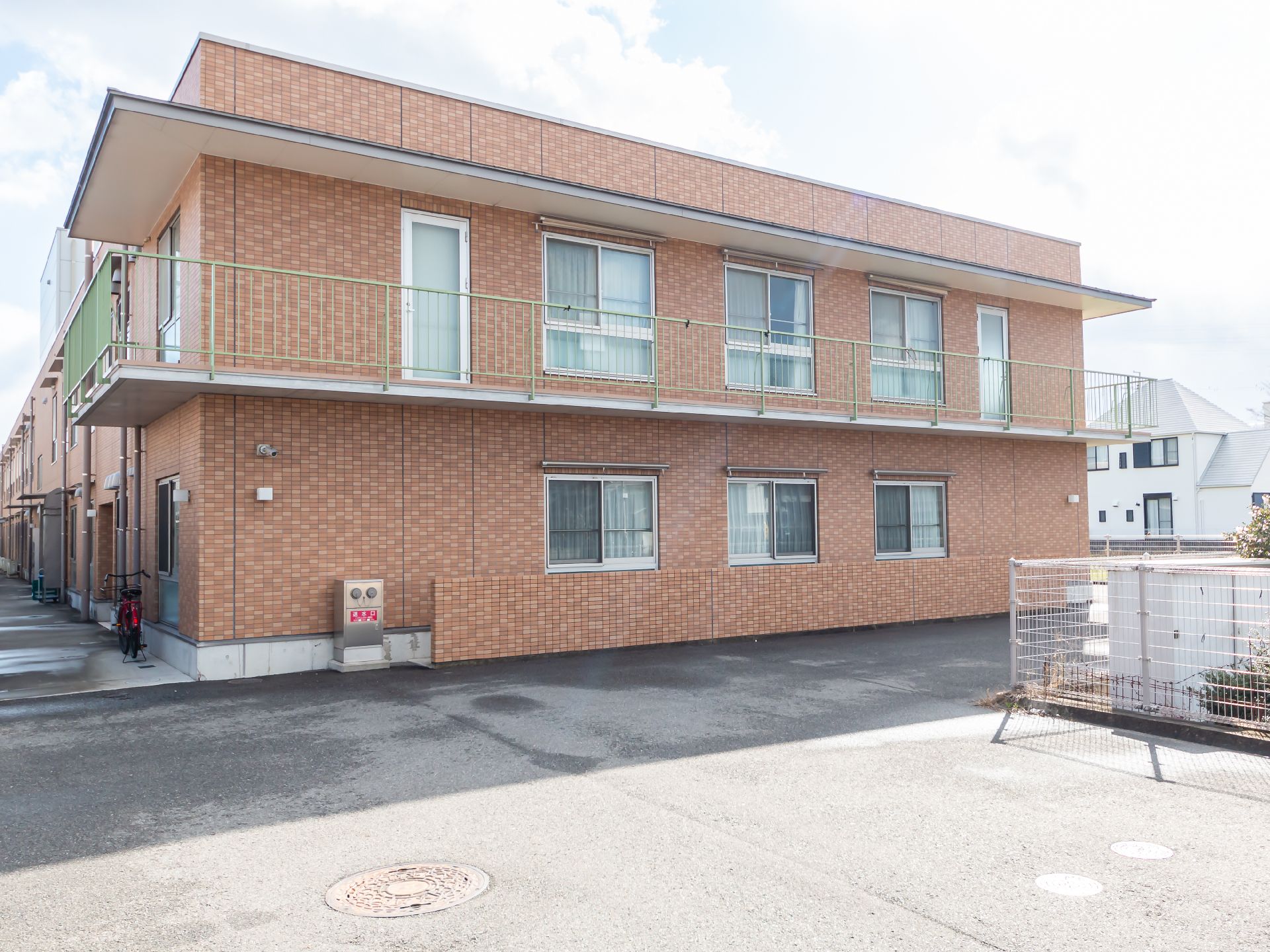 ブラウン系の2階建ての建物。広い敷地内には駐車場もあり、門には赤い文字で住宅名が書かれている。