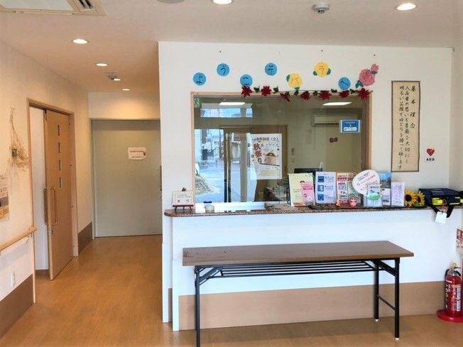 フロントの前には折り畳みの長机が設置され、うちわやパンフレットが並び、左側には廊下が続いている。消火器も設置されている。