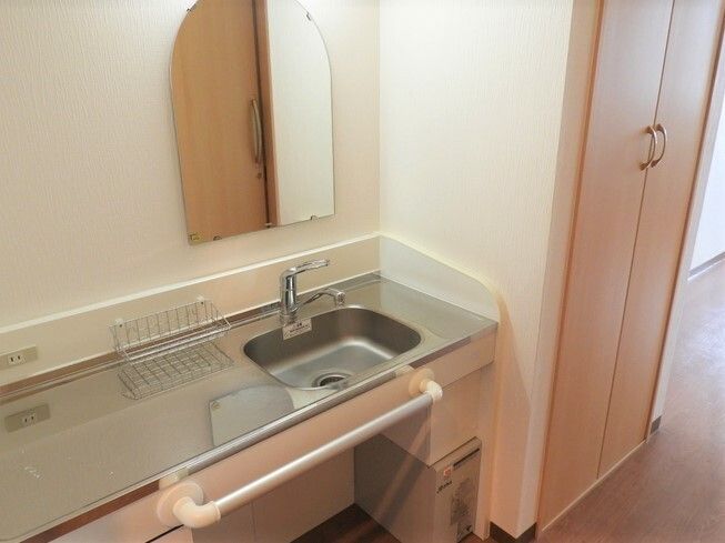 鏡が付いたステンレス製の寝具が付いた居室。作業台が広く、スポンジなどを置く小さなラックもある。シンクの右側には収納スペースもある。