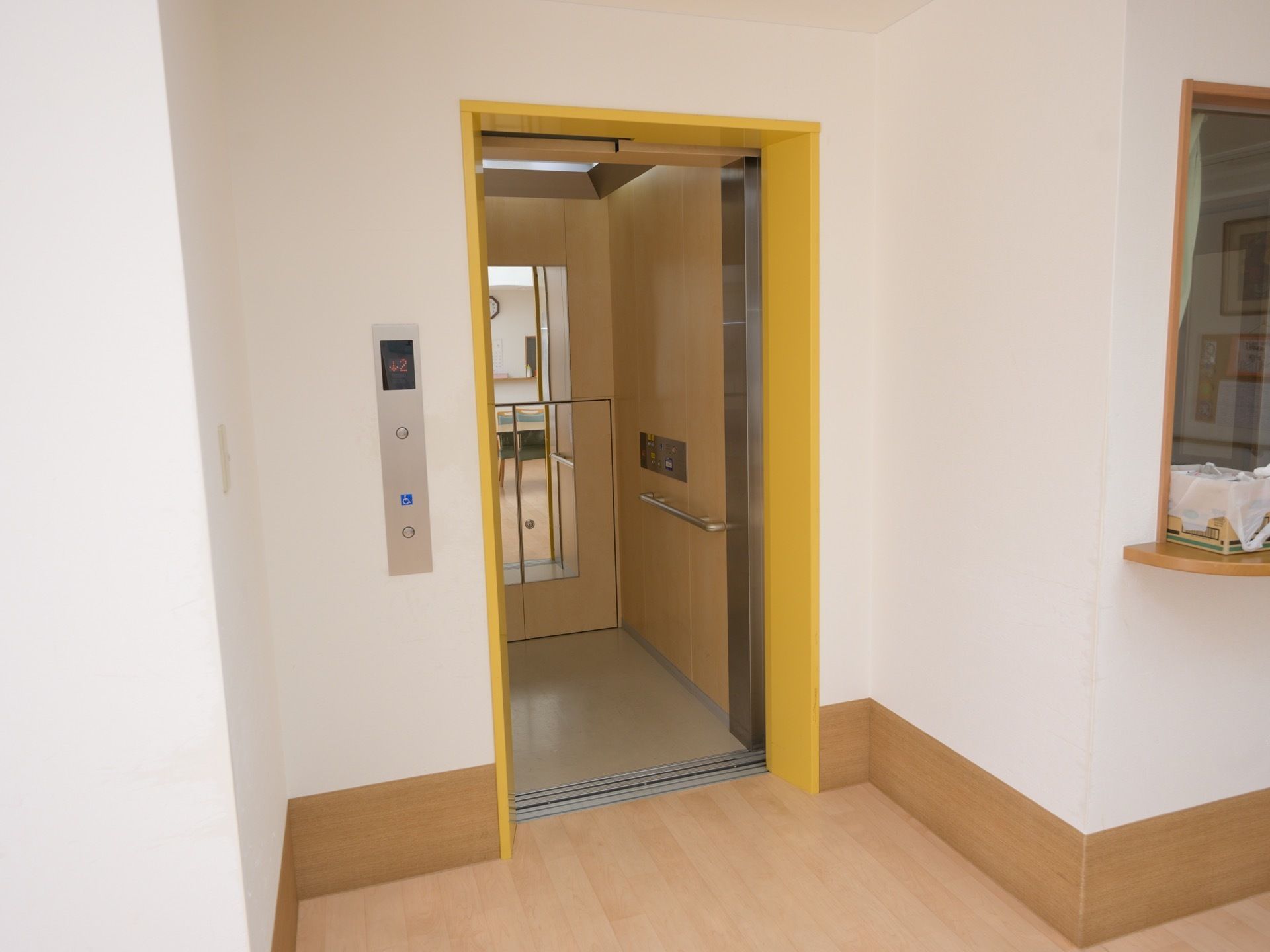 館内に完備されているエレベーターである。扉は開かれており、庫内に鏡が設置され木目調の壁が施されている。
