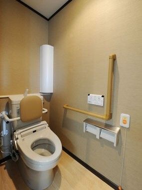背もたれと手すり付きのトイレには呼び出しボタンが設置され、操作パネルが壁にある。