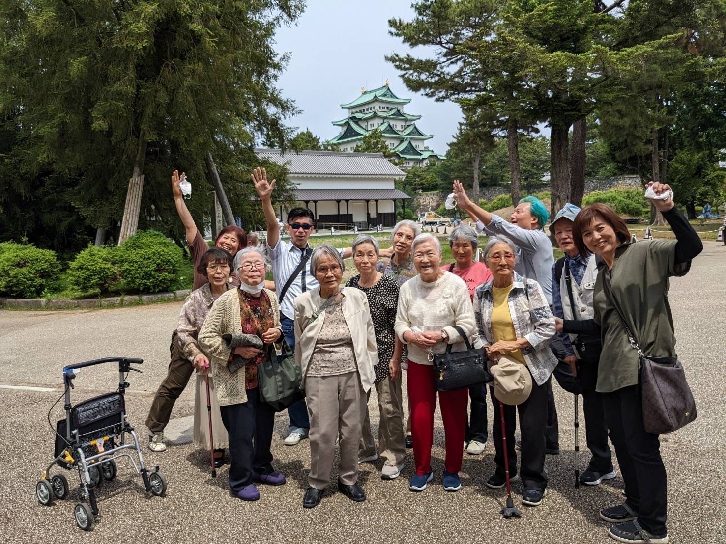 スタッフが数名付き添い、外出を楽しんでいる様子。周りには緑が多く、奥には和風の建物がある。