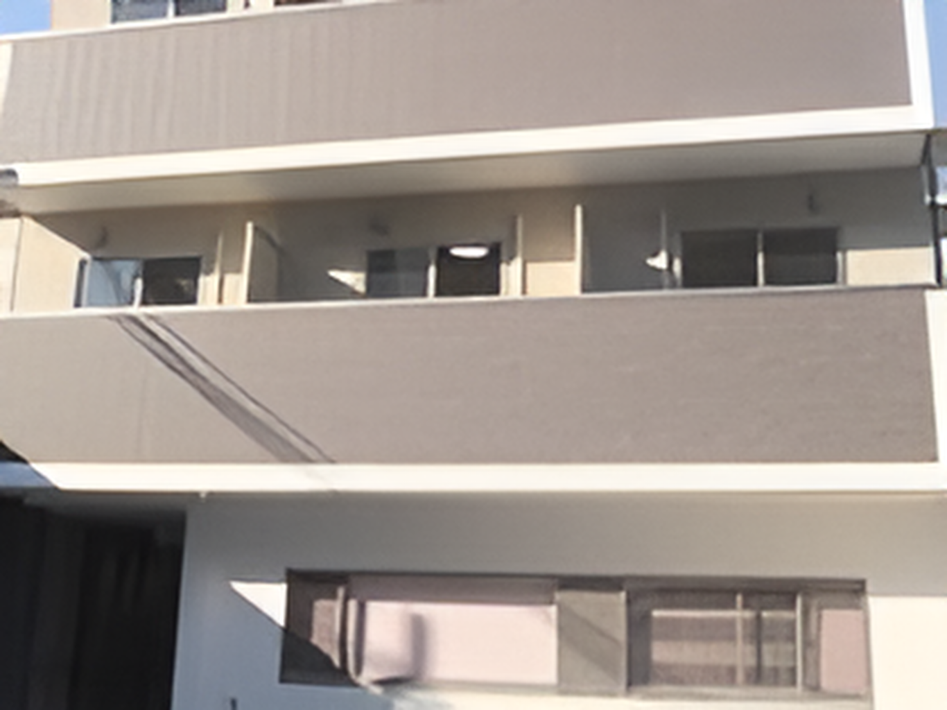 ブラウン系の外壁の3階建ての建物の一部。各フロアにベランダがあり、日当たりのいい場所に建っている。