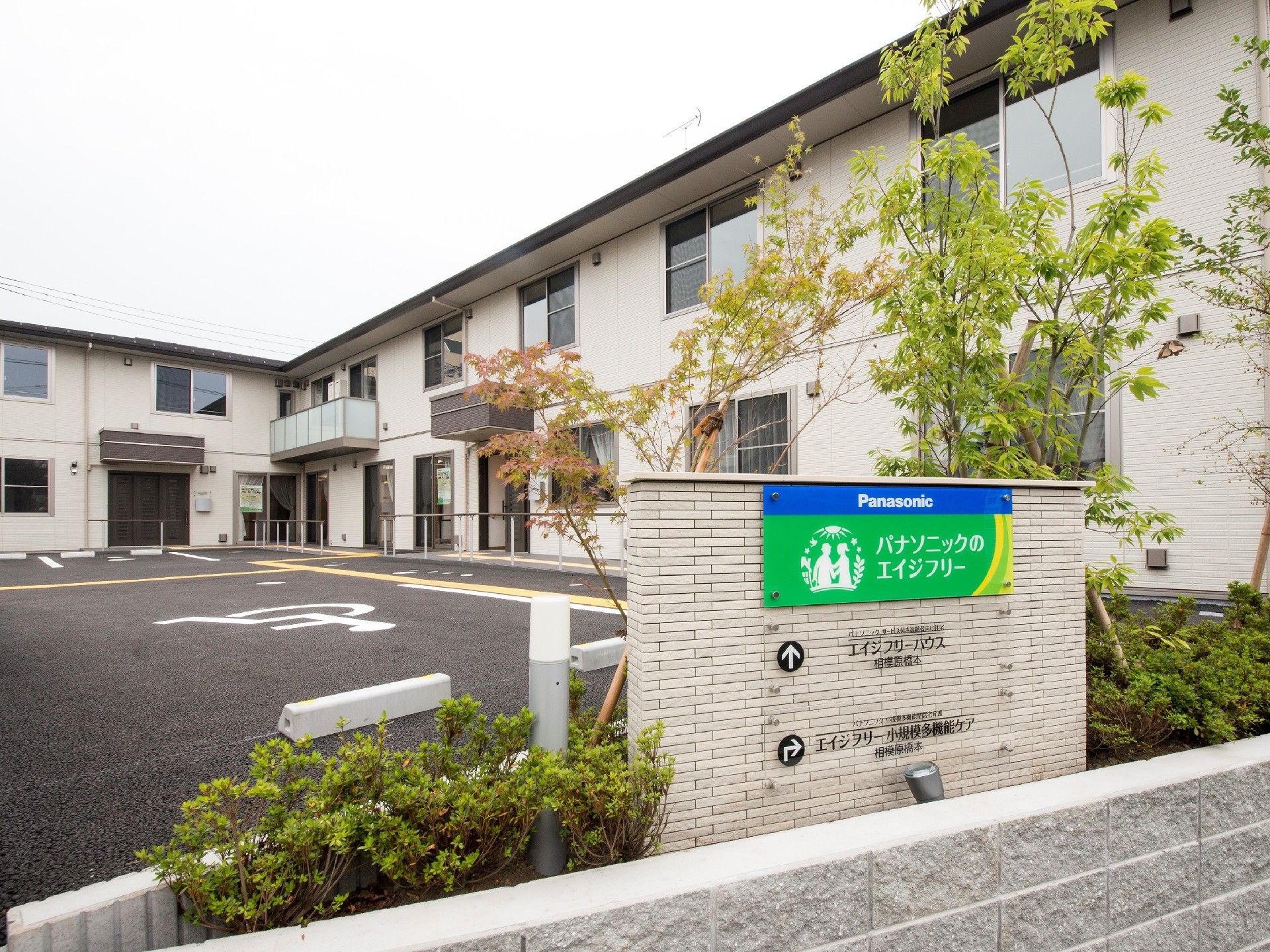 エル字型の建物は2階建てで広い駐車場が付き、周辺には木が植えられている。
