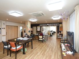 広い食堂に、テーブルが間隔を空けて置かれている。窓際にテレビがある。入居者様がお茶を飲みながら新聞を読んでいる。