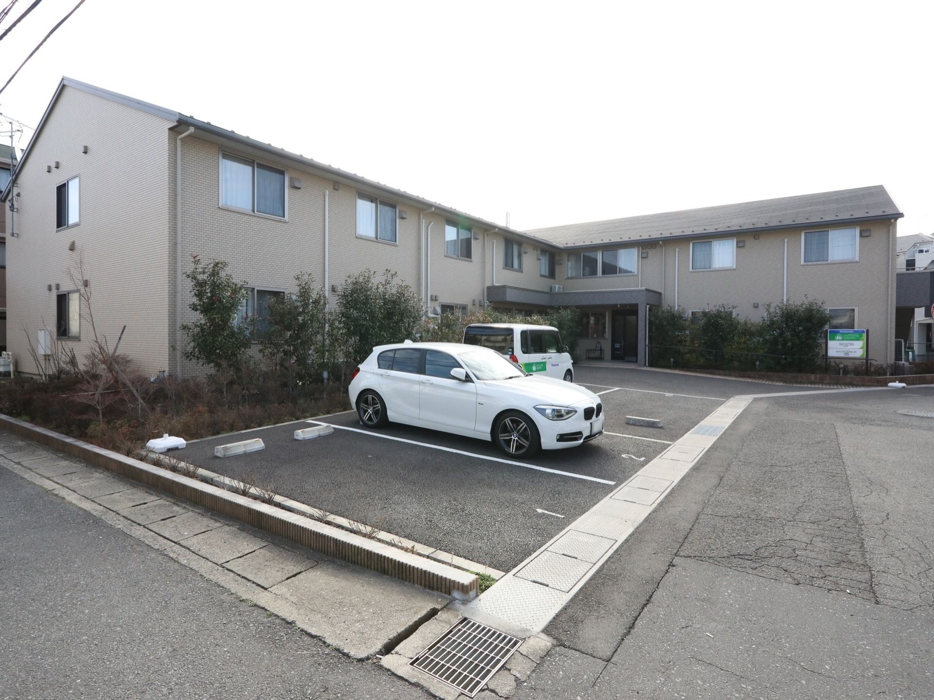 敷地内に白線で仕切られた駐車スペースがある。車止めが置かれている。建物と駐車スペースの間には植栽がある。