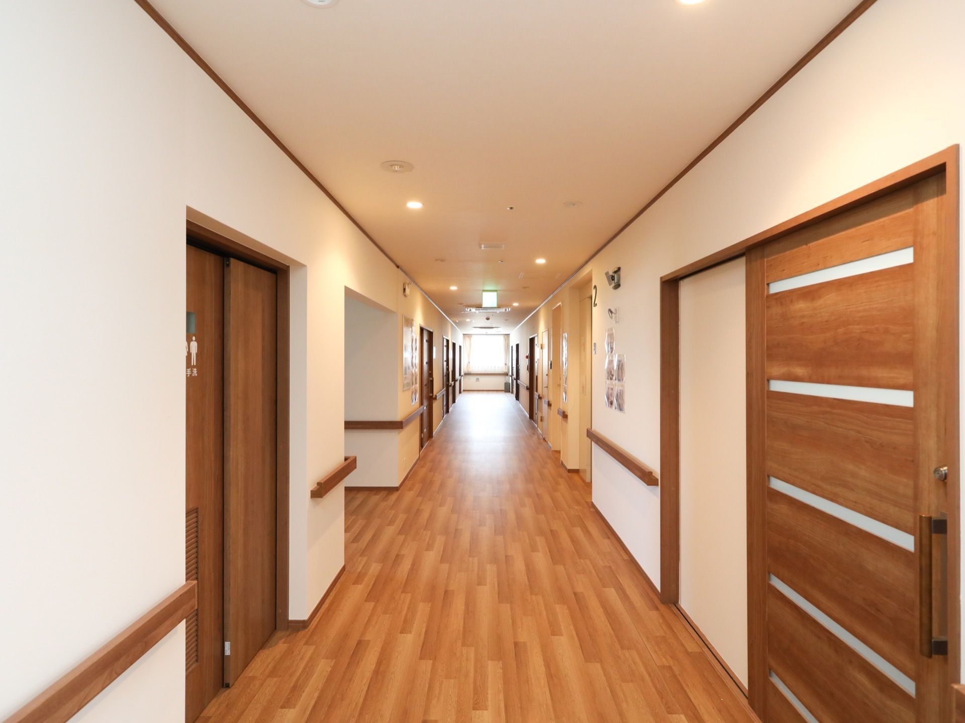 白色と茶色を基調としたきれいな廊下である。板状の手すりが両側の壁に設置されている。共同トイレの入口扉がある。
