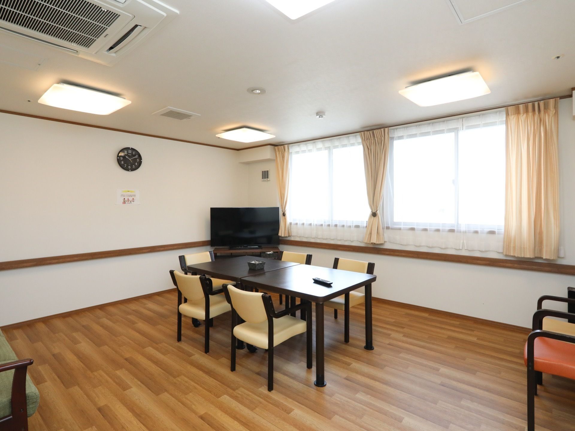 テーブルや椅子を備えた休憩スペースが設けられている。部屋の隅にテレビが置かれている。天井埋め込み式のエアコンが設置されている。