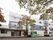 白とグレーの３階建ての建物。玄関先には看板があり、木も植えられている。