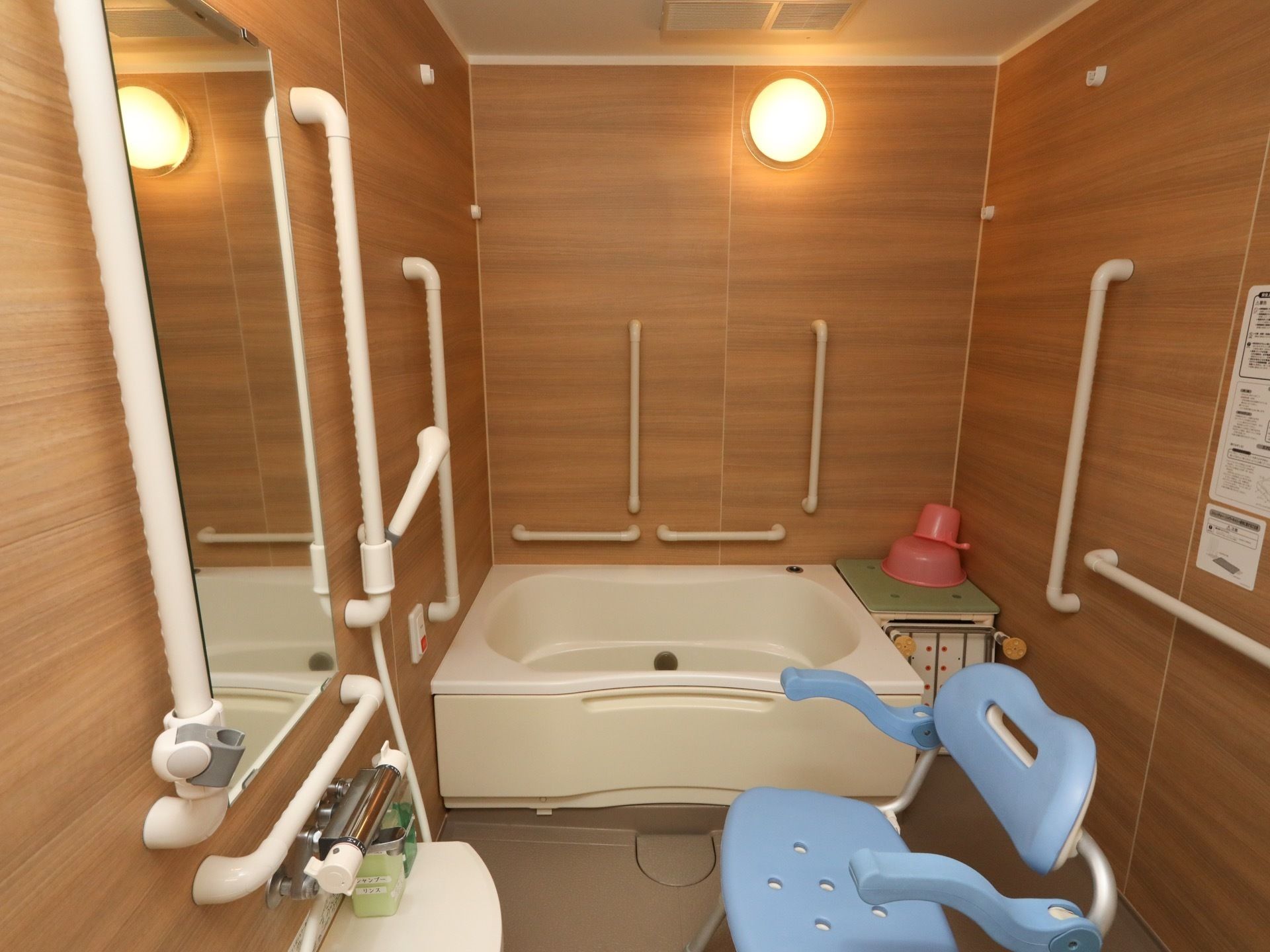 浴室は木目調の壁を採用しており、あたたかみが感じられる雰囲気。壁には手すりが多数設置されて、シャワーチェアーや踏み台なども完備されている。