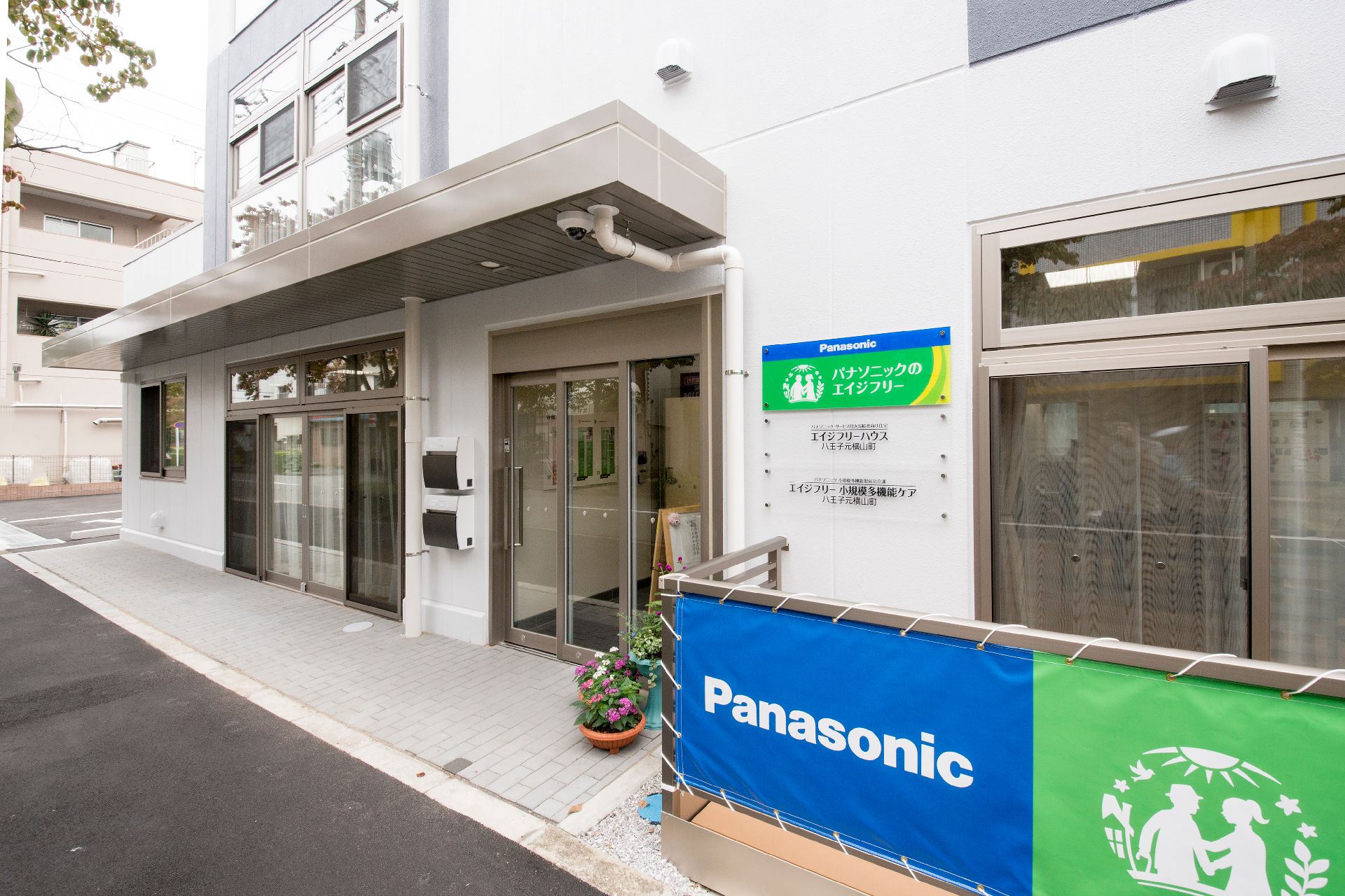 屋根が付いた玄関には自動ドアが付き、事業所の名前が書かれたプレートが飾られている。
