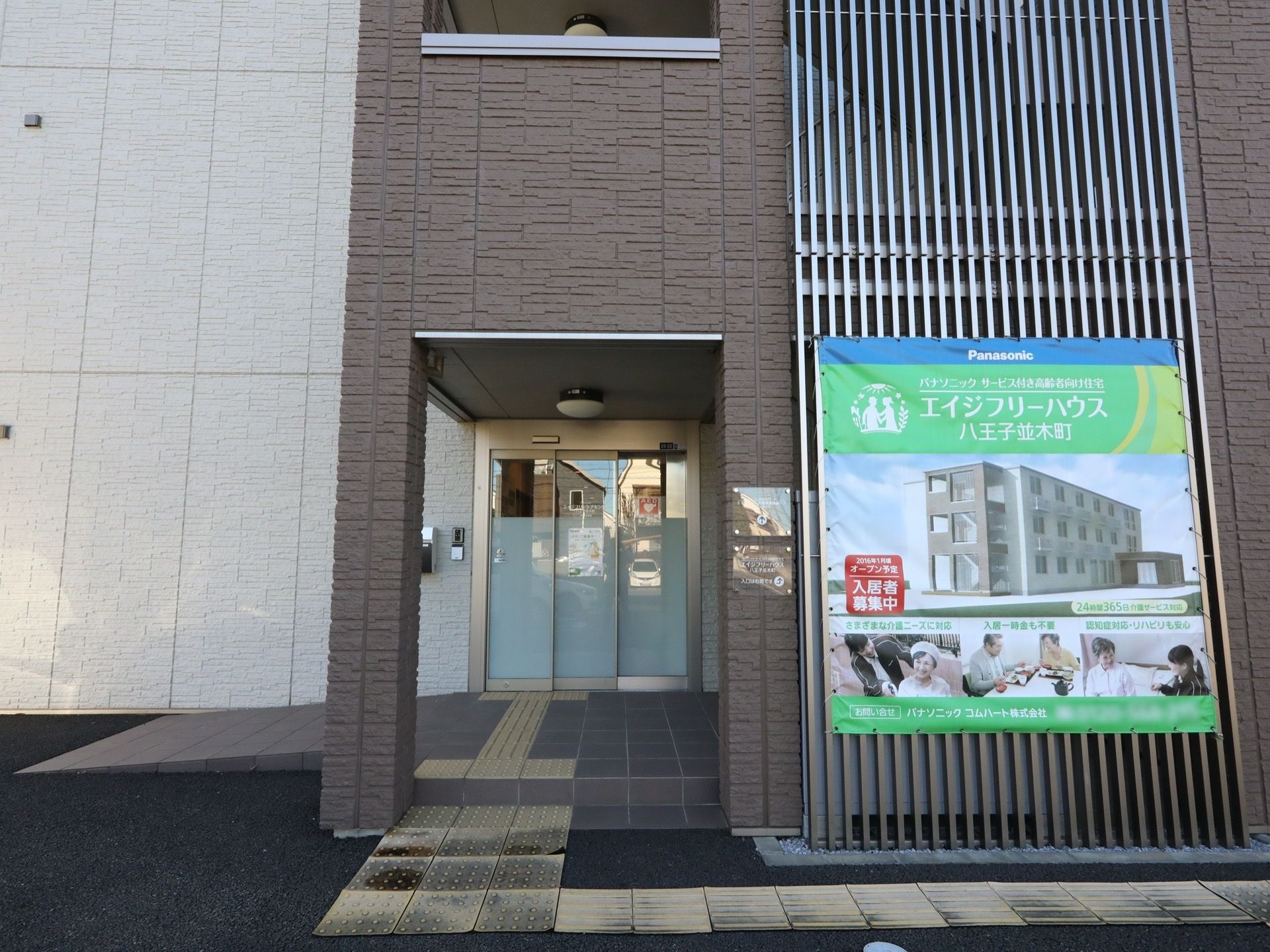 玄関から外まで、点字ブロックが敷き詰められている。壁には、施設の写真とともに入居者募集と書かれた旗が付いている。