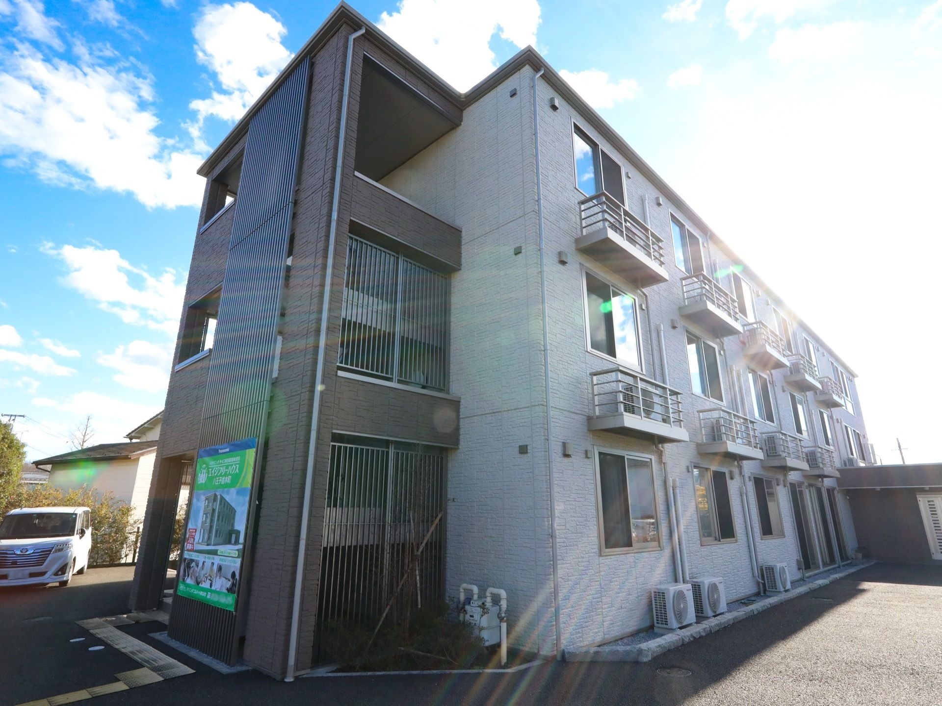建物の玄関側に、外階段が設置されている。2階と3階のそれぞれの窓の下に、室外機が取り付けられている。