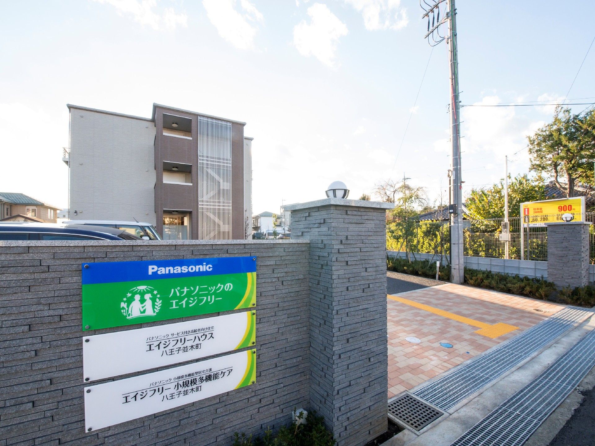 3階建ての建物は広い敷地になっていて、周辺には緑も多く、門には住宅と併設事業所の名前が書かれている。