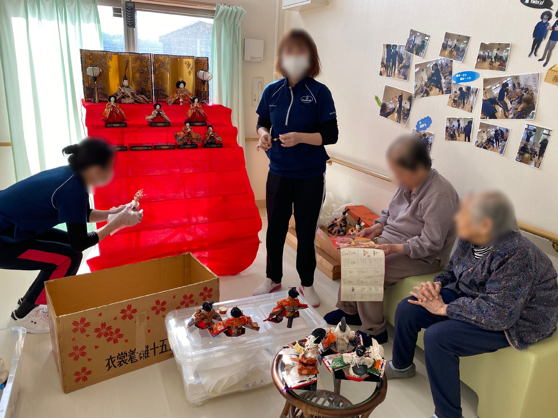 車いすの高齢女性と付き添いの高齢男性の両サイドには若い男女のスタッフが笑って立っている。