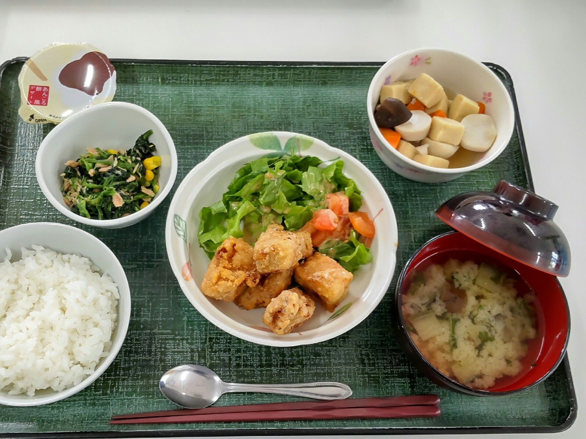 生野菜が添えられた唐揚げをメインに、白いご飯に味噌汁、野菜の煮物やあえ物が添えられ、デザートも付いた食事。