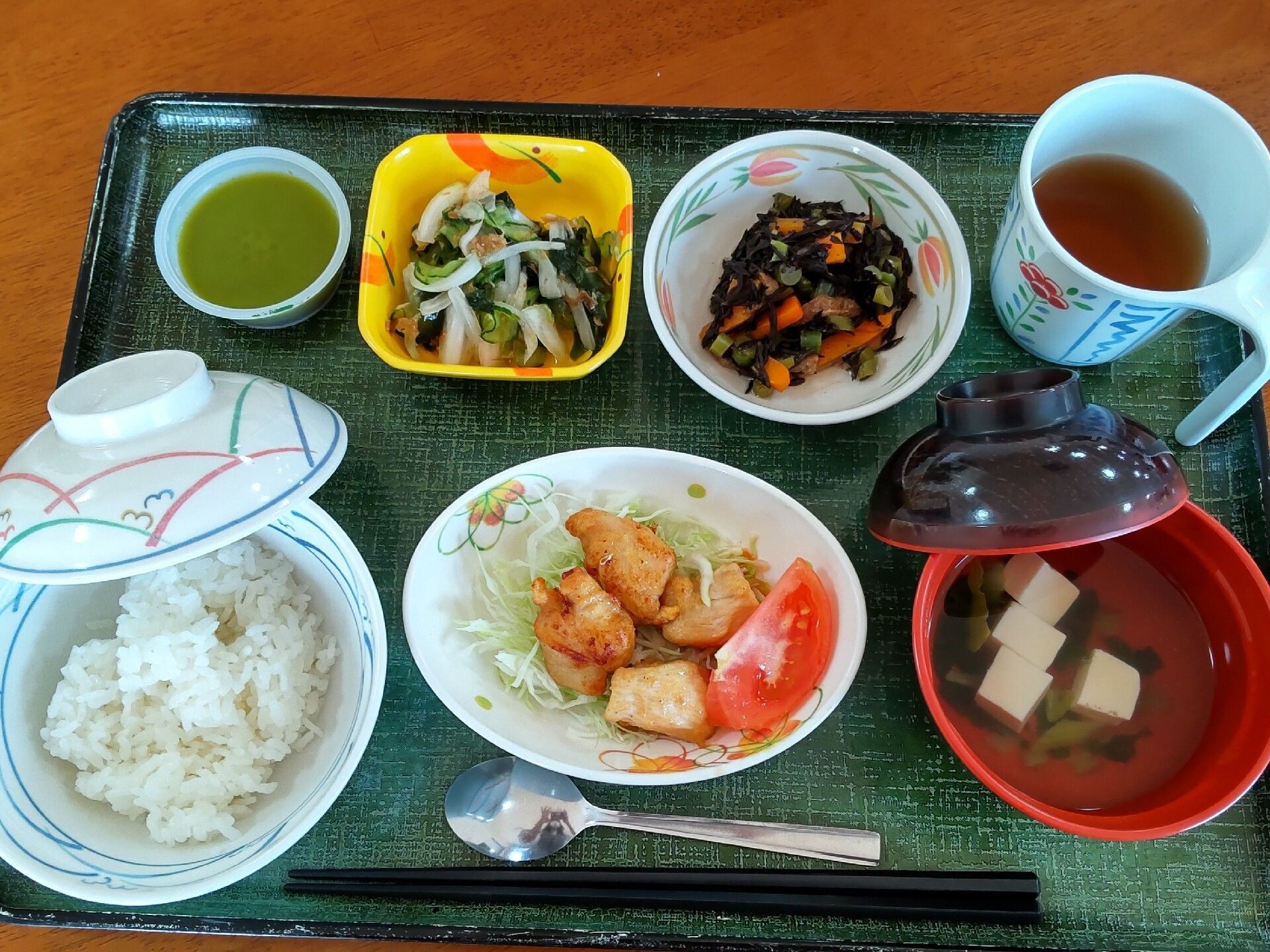 白いご飯や汁物、生野菜が添えられた揚げ物、ヒジキ、酢の物などにお茶が添えられている。