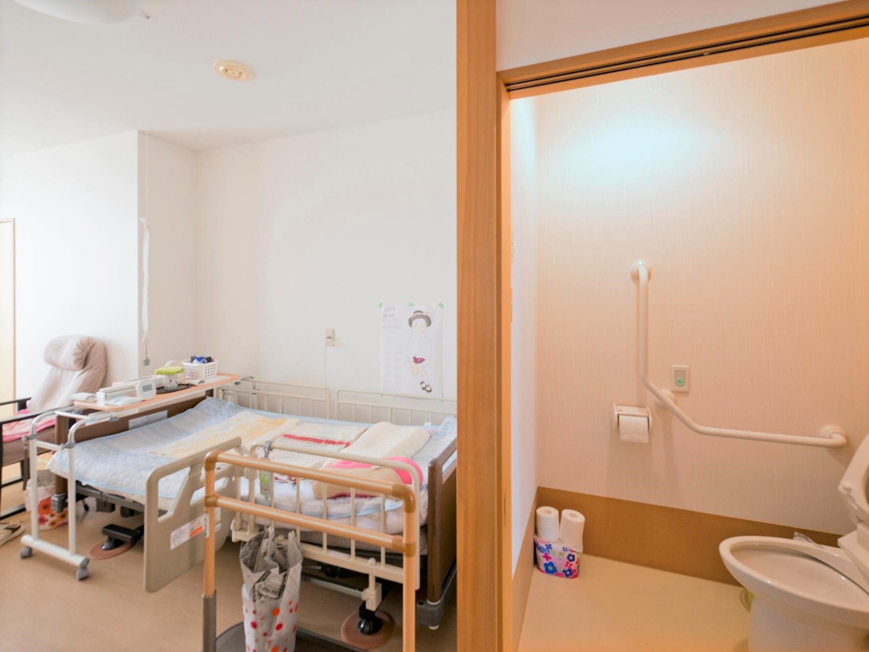 ベッドサイドには緊急通報装置があり、トイレの中には手すりがある。いすなどの私物も持ち込まれた居室。