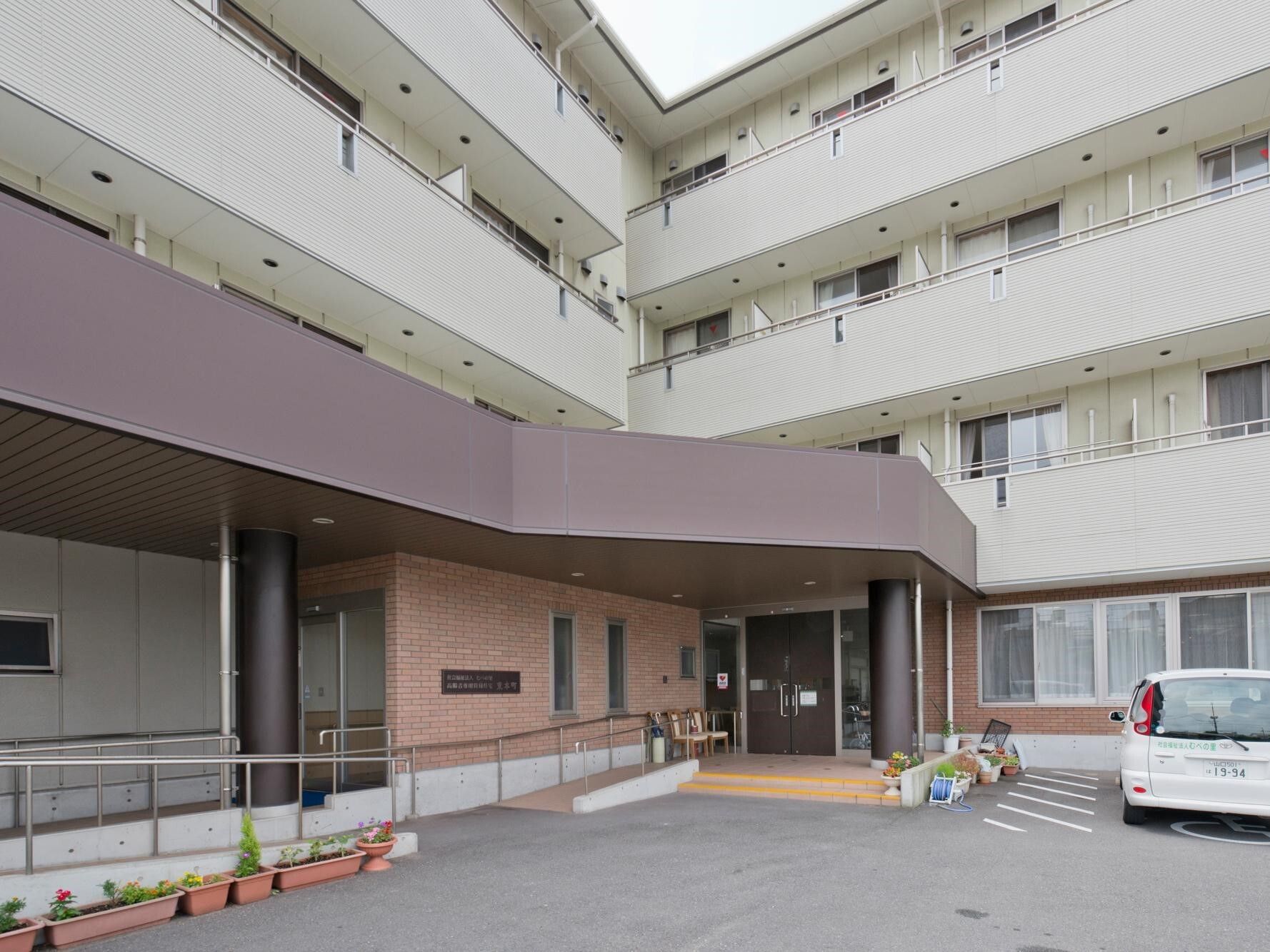 手すり付きのスロープが付いたホーム。ホワイト系で各フロアにベランダがあり、玄関には屋根が付いている。