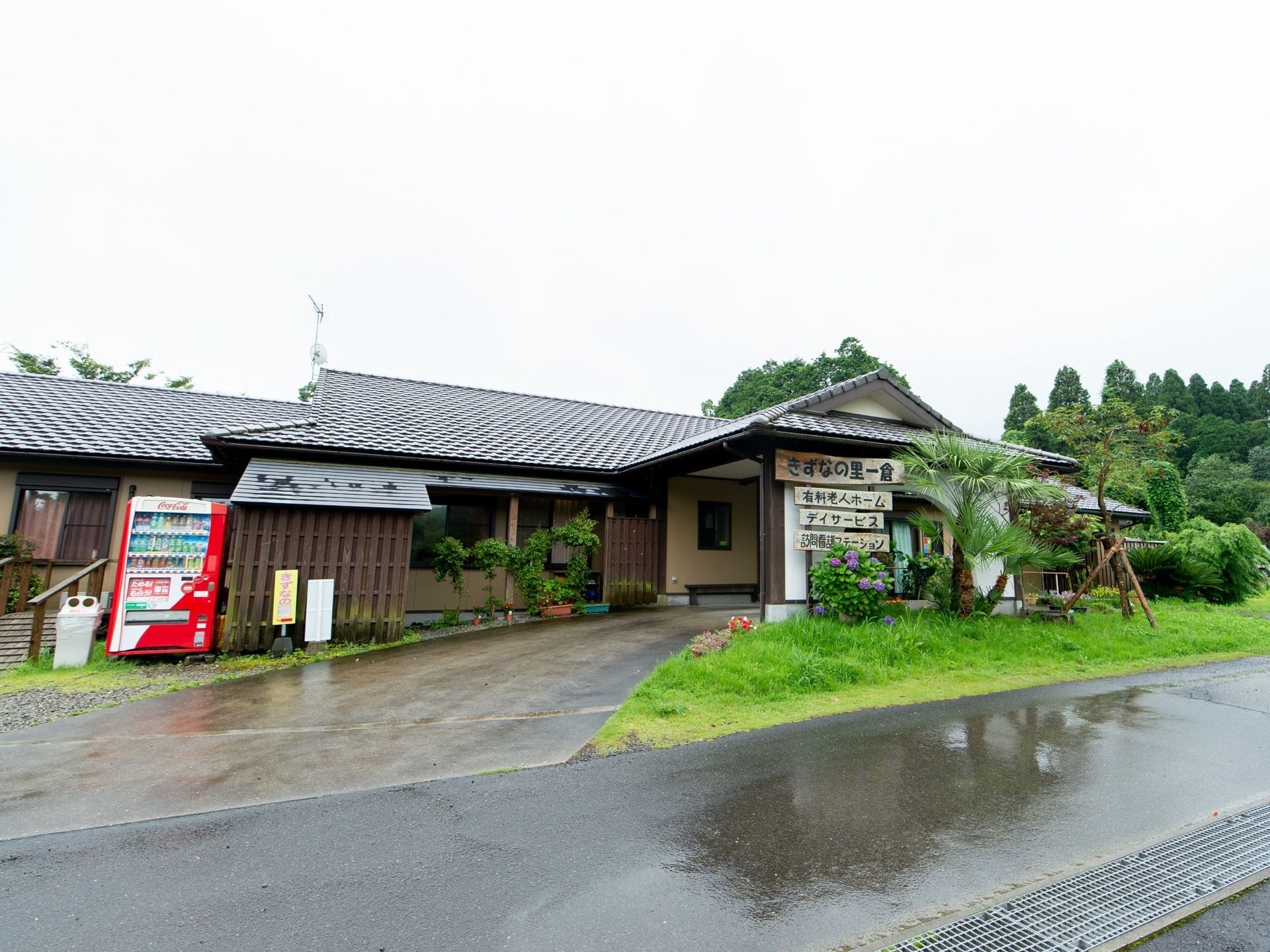 瓦屋根の建物で、玄関の上は三角の屋根になっている。道路から玄関にかけて緩やかなスロープになっており、左の方には自動販売機が設置されている。