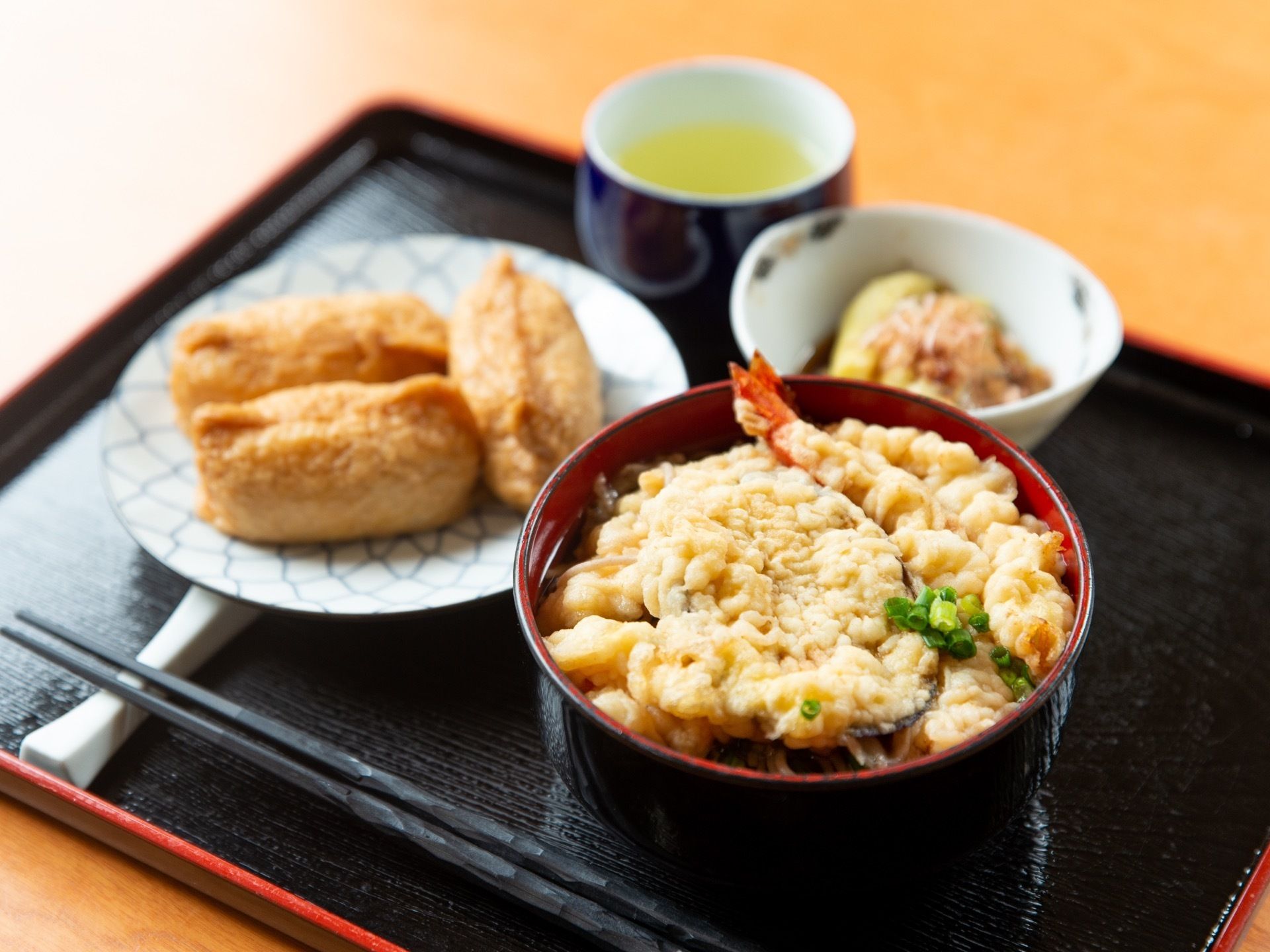 黒いトレーに天ぷらそばやいなり寿司、お茶などが並べられている。白い箸置きに、黒いお箸が置かれている。