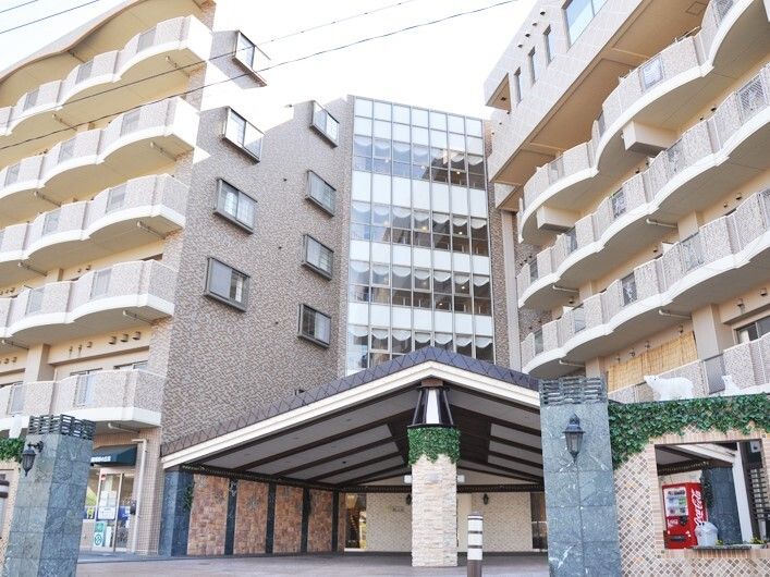 白とグレーの大きな建物。自動販売機が置かれ、玄関には大きな屋根がある。