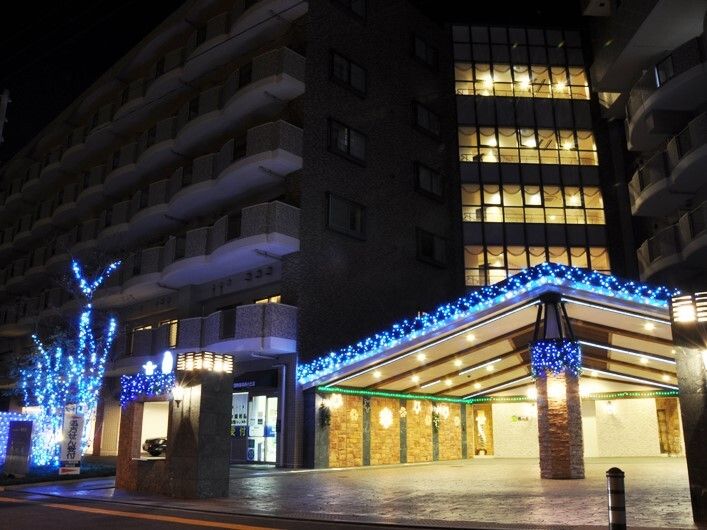 夜になりあたりが暗くなっているが玄関周りは明るく、玄関の屋根や近くにある木はブルーのライトで飾られている。