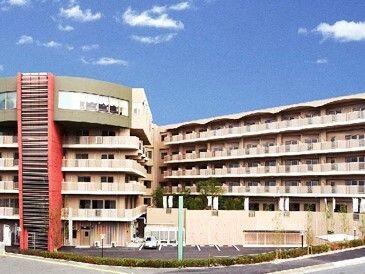 ベージュ系の大きな建物は各フロアにベランダが付き、少し変わったエル字型となっていて、駐車スペースもある。