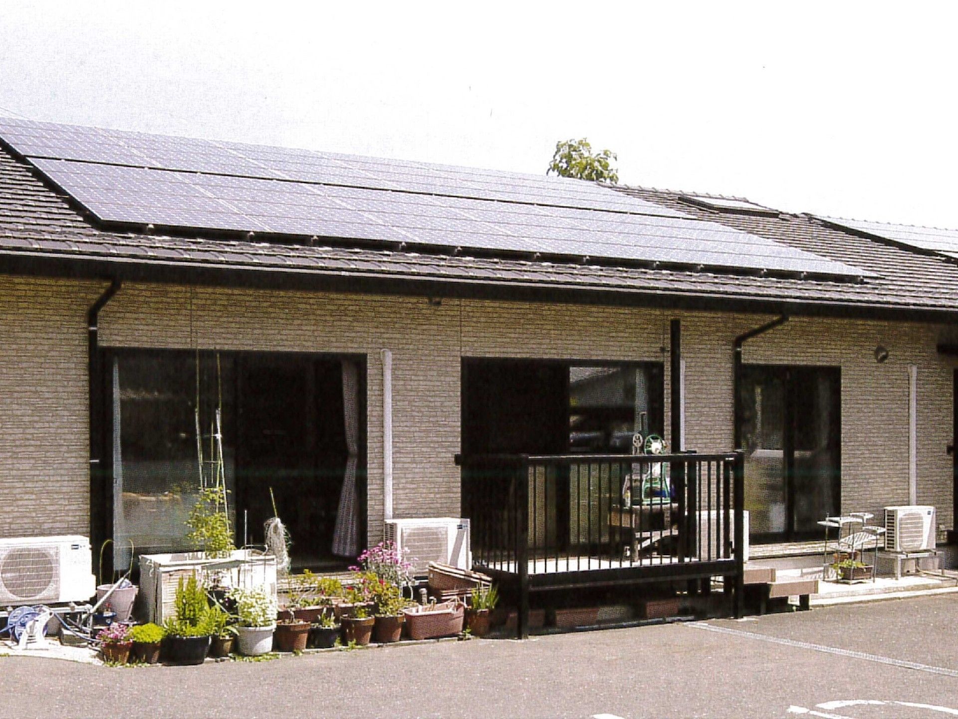 平屋建てのベージュの建物。ウッドデッキも付き、鉢植えもある。
