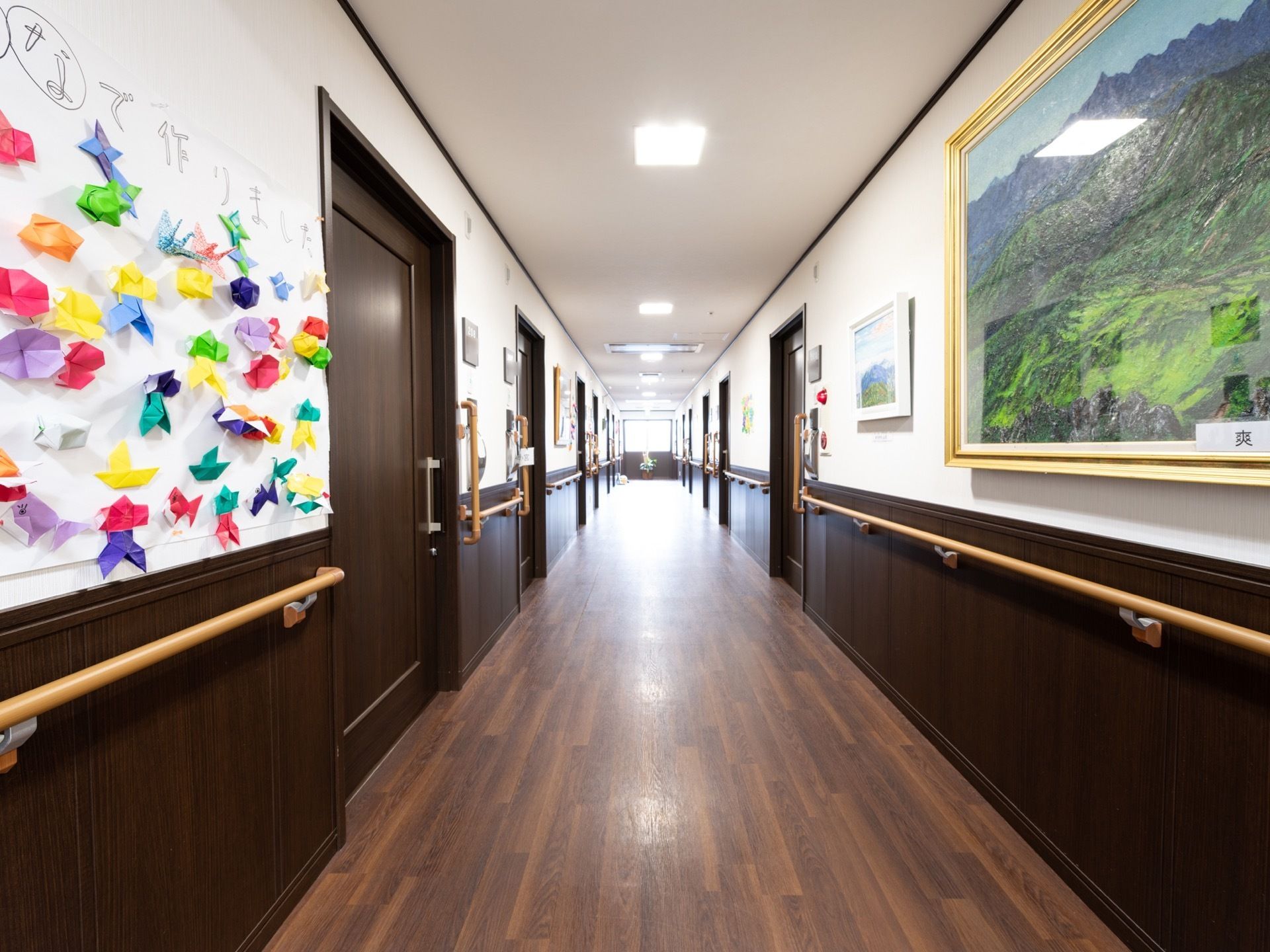居室の扉が並ぶ廊下には、絵画や折り紙で作られたアイティムが飾られている。ダークブラウンの床の落ち着いた内装である。