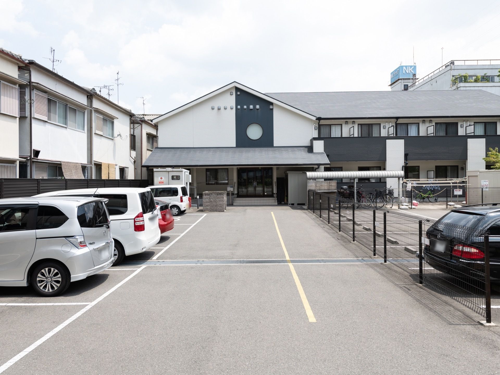 大きな三角屋根と丸い窓が印象的なモダンな外観である。正面玄関前には、駐車スペースが広くとられている。