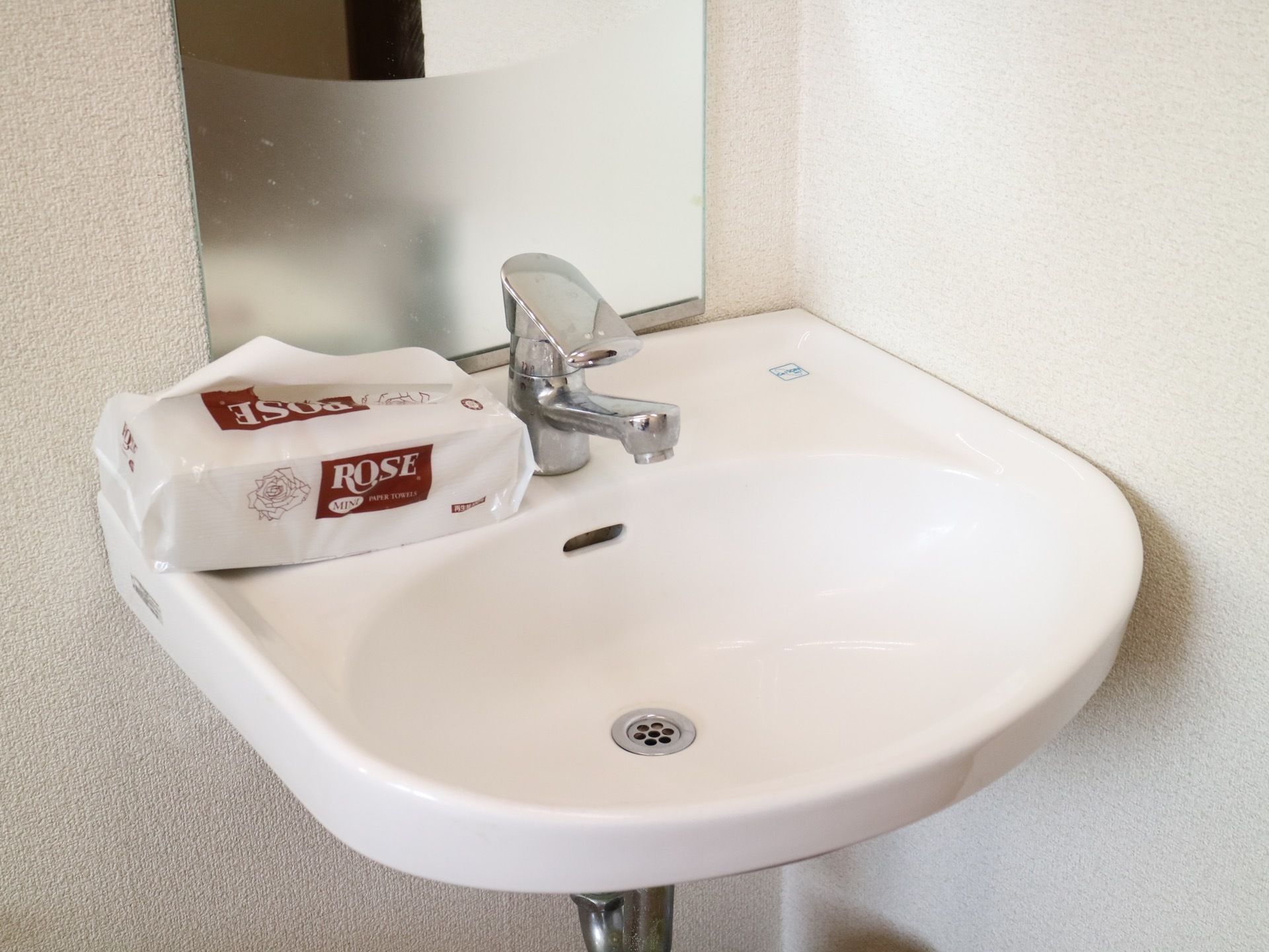 レバー引き上げ式の水栓がついた洗面台が設置されている。水栓の左側に、ビニールの袋に入ったペーパータオルが置かれている。
