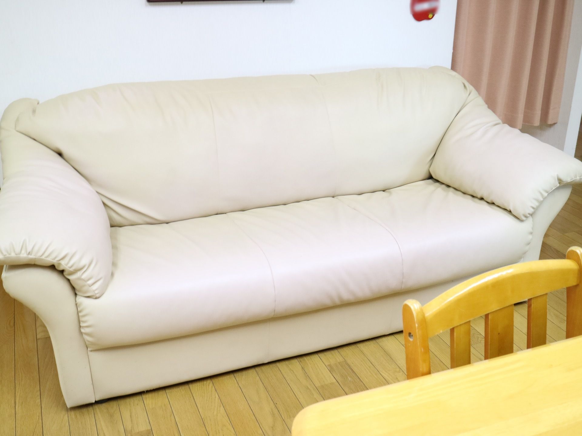 白色のカバーの大きなソファが壁につけて設置されている。その近くに、明るい色の天板のテーブルがある。
